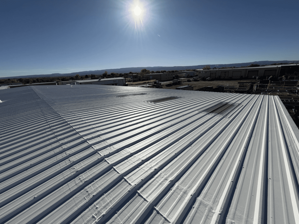 Large white metal rooftop under bright sun with clear blue sky; rows of industrial buildings and distant mountains visible in the background.